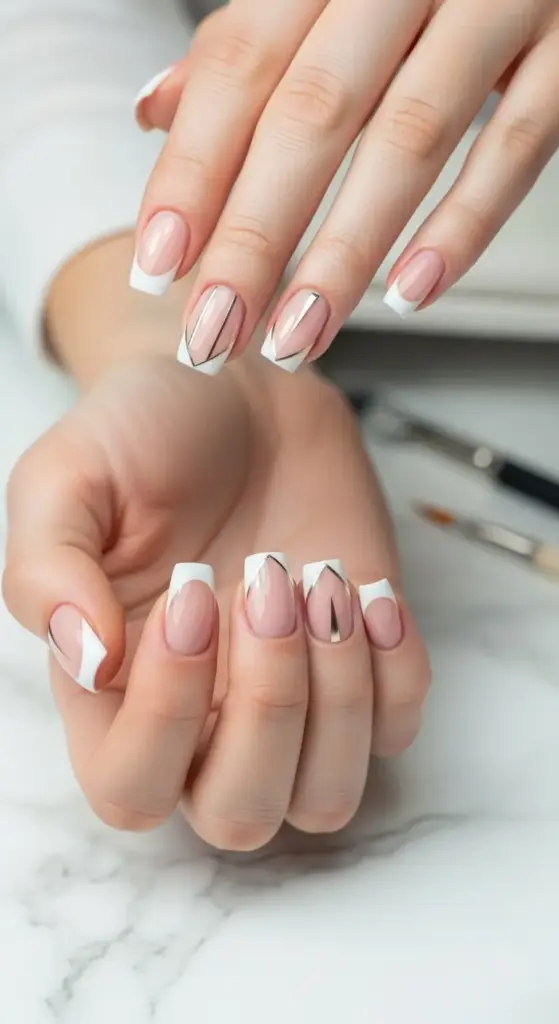 Stylish and modern French manicure on short acrylic nails. The nails feature a classic white tip design with unique geometric lines in metallic gold and silver, creating a chic and sophisticated look. The hands are posed against a white marble background with nail art tools in the background.
