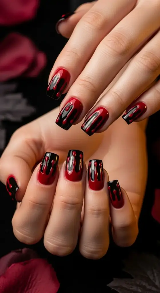 Short square nails with a glossy black base and a bloody red dripping design, creating a vampire-inspired look. These Spooky Halloween Nails are set against a dark background with blurred red rose petals.
