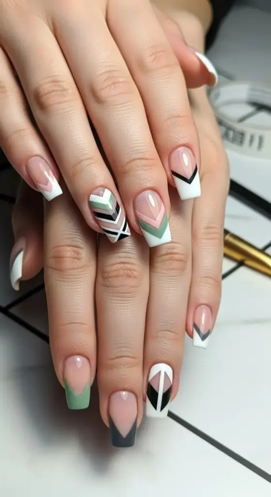 This striking image features a unique take on French tip acrylic nails, showcasing a geometric design. The nails are medium-length and a squared-off coffin shape. While some nails have a classic white French tip, others feature intricate patterns with chevrons and triangles in a palette of sage green, black, and white. This creative and modern manicure shows how French tip acrylic nails can be customized with artistic flair.