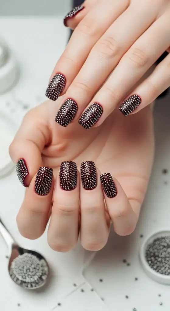 Glamorous manicure featuring shiny dark red nails completely covered in tiny silver studs for a caviar nail art look.