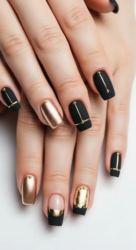 Trendy hands with a high-fashion manicure featuring matte black nails, glossy gold accents, and a variety of metallic gold geometric designs, including abstract black french tip nails and accent nails with gold foil and studs.